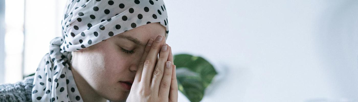 Eine Frau im Gebet. Sie trägt ein Kopftuch wie nach einer Chemotherapie.