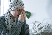 Eine Frau im Gebet. Sie trägt ein Kopftuch wie nach einer Chemotherapie.